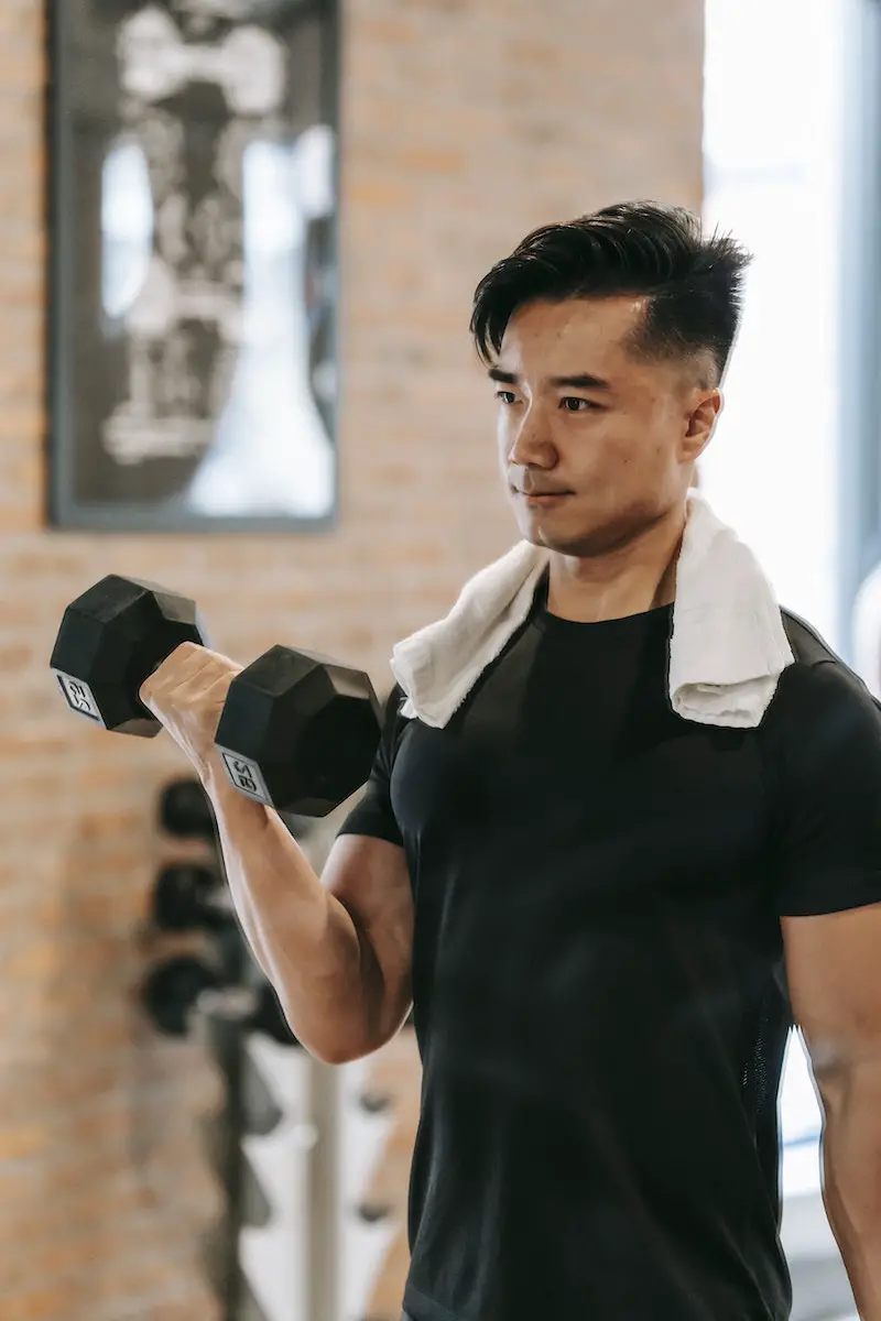 Muscular Asian man training with dumbbell